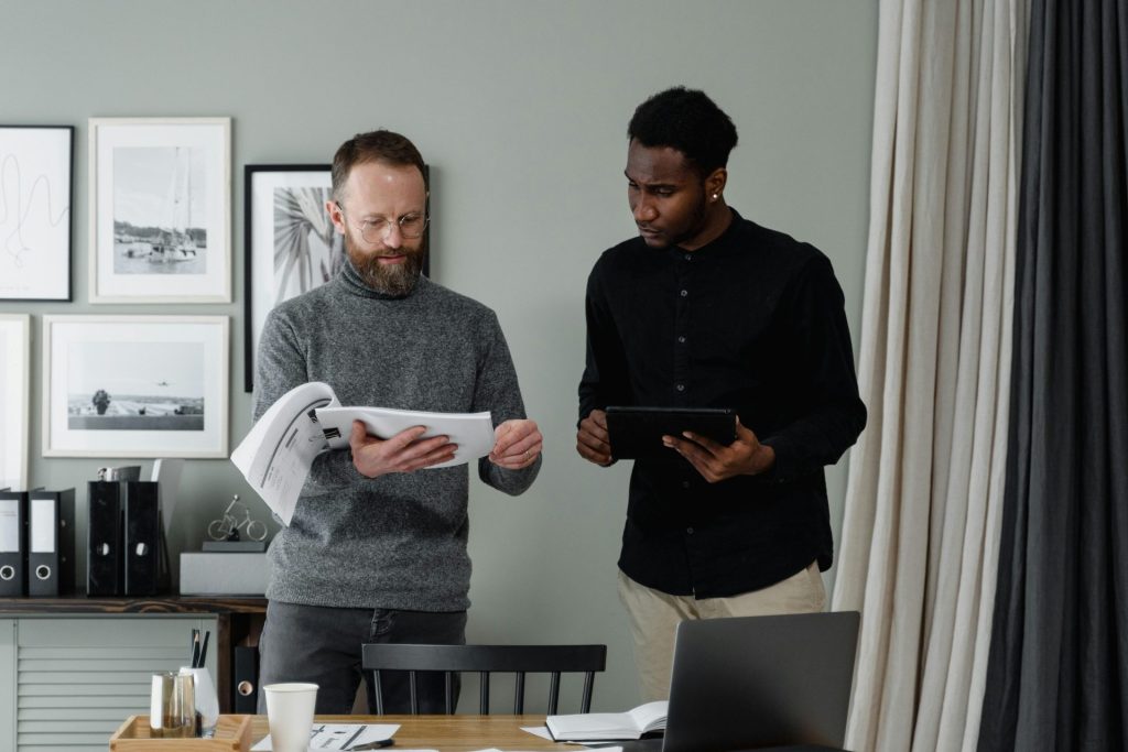 Two professionals reviewing documents and using a tablet in a modern office setting.