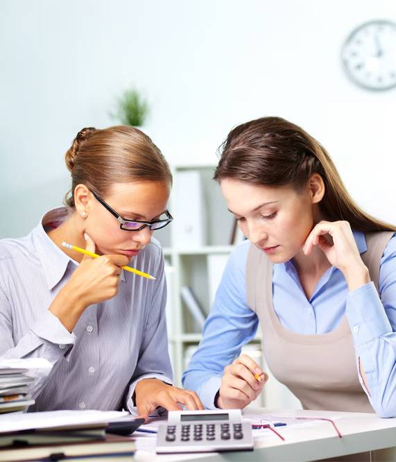 Two women analyzing documents with a calculator.